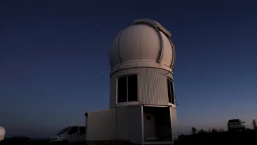 Astronomical observatory under a starry sky at dusk, with a parked van nearby.