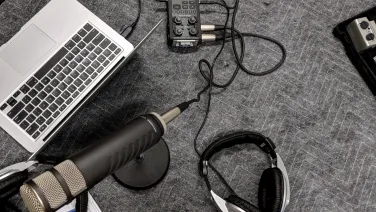 A laptop, microphone, headphones, and audio mixer on a textured gray surface, suggesting a podcast or recording setup.